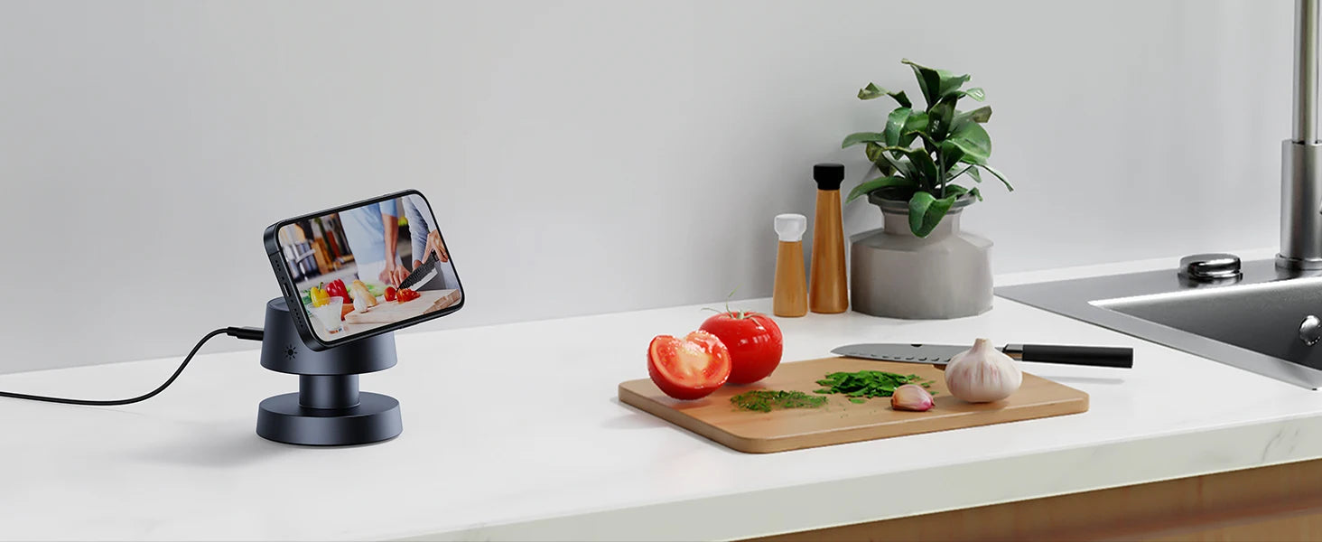 Smartphone on 4-in-1-charger displaying a cooking app over a kitchen counter with vegetables and a cutting board.
